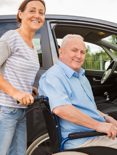 Smiling senior man in a wheelchair in front of a silver car